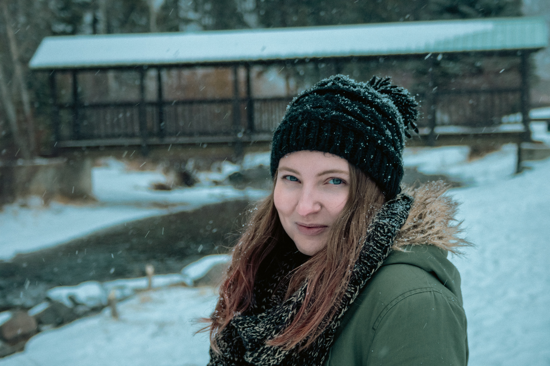 A girl with long hair stands in the snow smiling warmly.